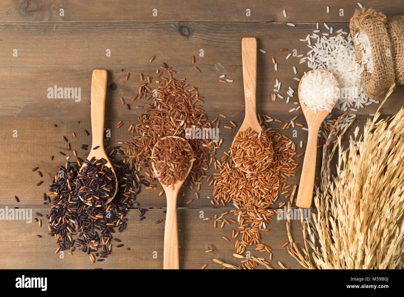 Row of white jasmine rice with various rice:  Rice berry, brown and thai red mixed rice on brown wooden background, organic rice and healthy food. Stock Photo