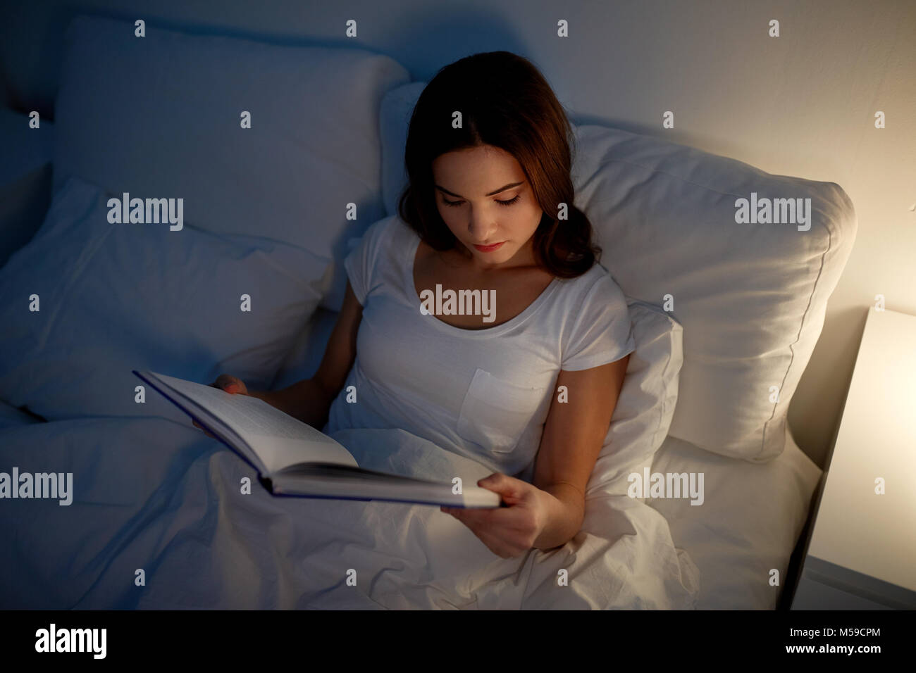 young woman reading book in bed at night home Stock Photo