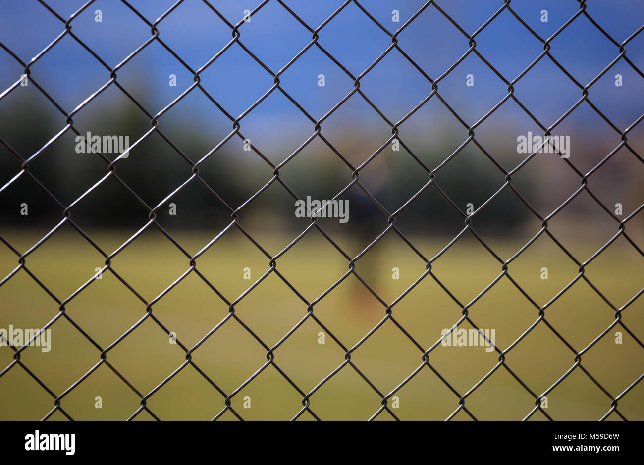 Wire metallic mesh fence around a football field. Blurred green grass ...