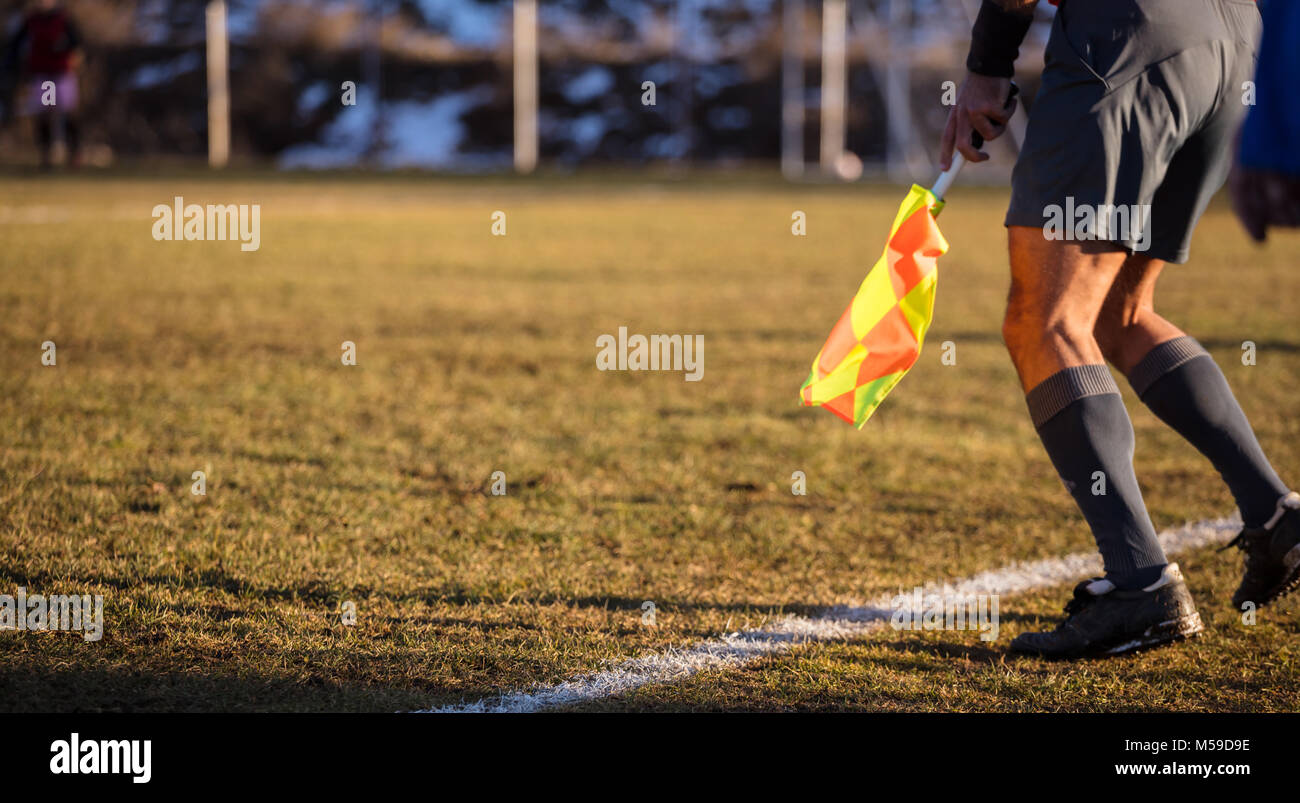 Football soccer arbiter assistant moves at sideline observing the match with flag at hands. Blurred green field and nature background, close up view,  Stock Photo