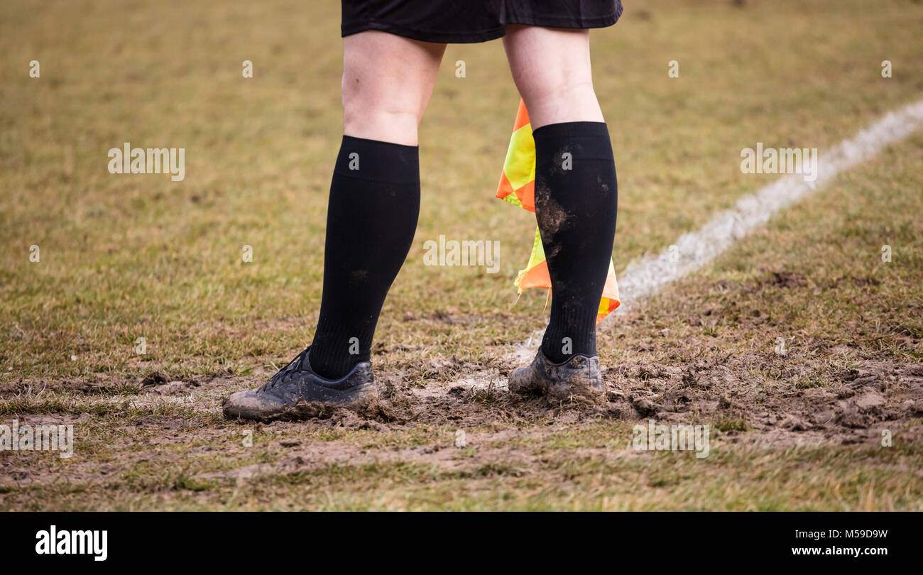 Football soccer arbiter assistant stands at corner side with shoes full of mud and flag at hands. Blur green field background, close up. Stock Photo
