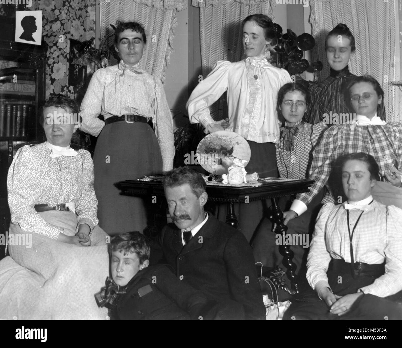 Family portrait in the parlor results in a bizarre look in their eyes due to ghosting and motion during glass negative exposure, ca. 1905. Stock Photo