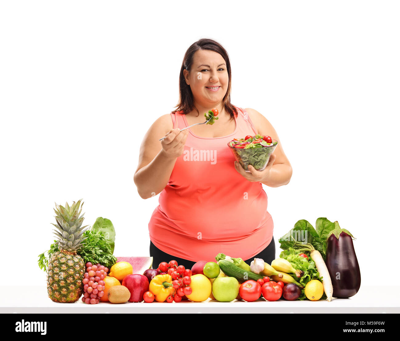 Overweight woman eating a salad behind a table with fruit and vegetables  isolated on white background Stock Photo - Alamy