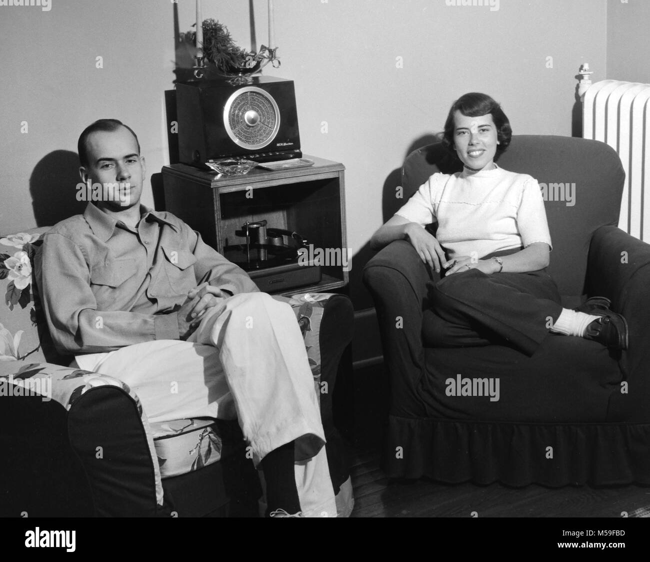 Young couple enjoy time in their living room with their radio and turntable sound system, ca. 1950. Stock Photo