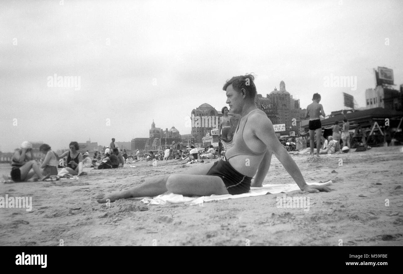 A man wears a stylish bathing suit with a man bra feature lounges in the sand in Atlantic City, New Jersey in 1939. Stock Photo