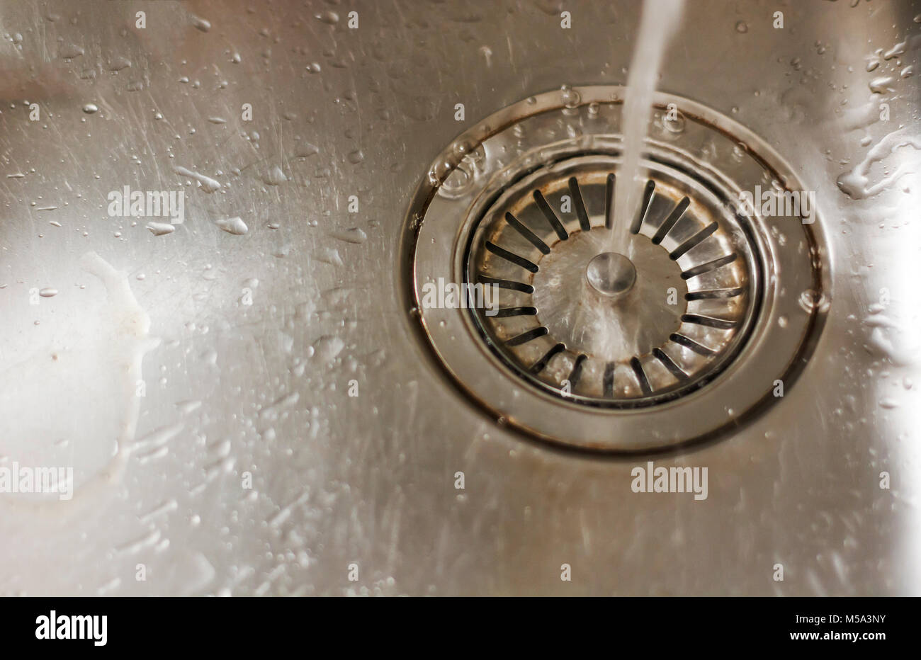 water falling on a steel sink plug hole Stock Photo