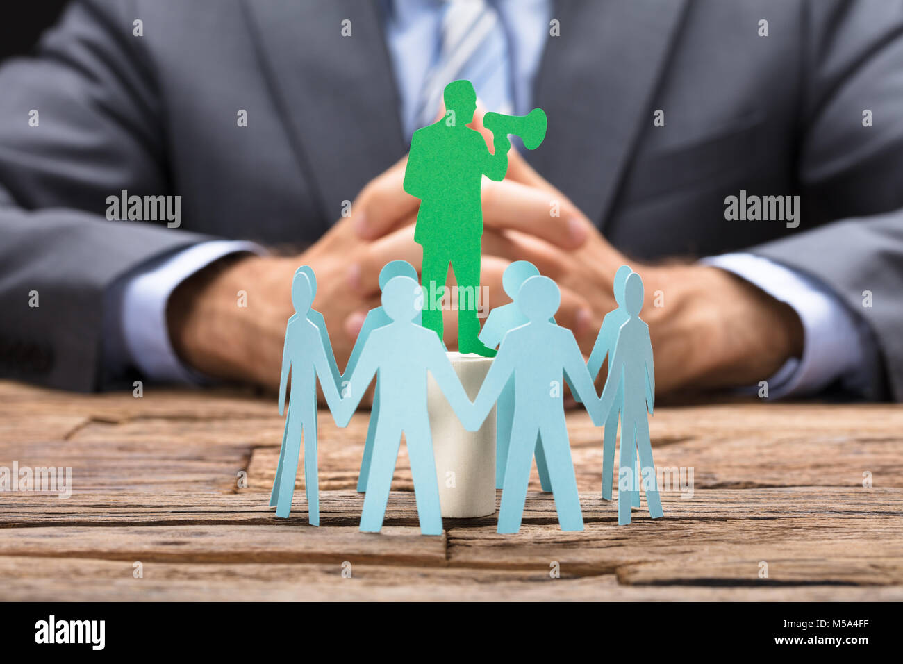 Green paper executive speaking through megaphone surrounded by team on