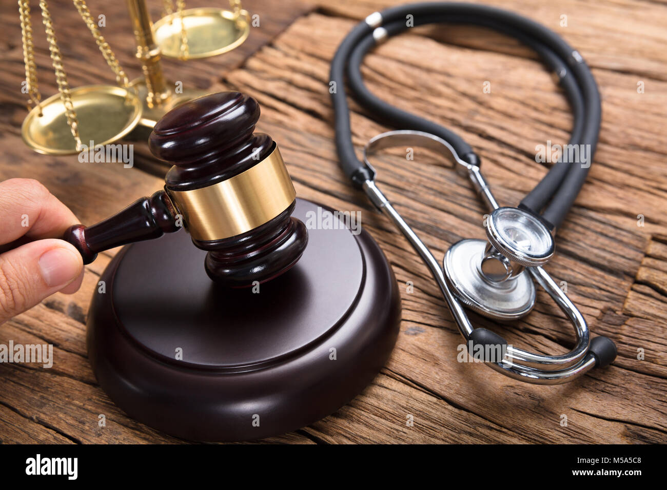 Judge hitting mallet by stethoscope and justice scale on wooden table in courtroom Stock Photo