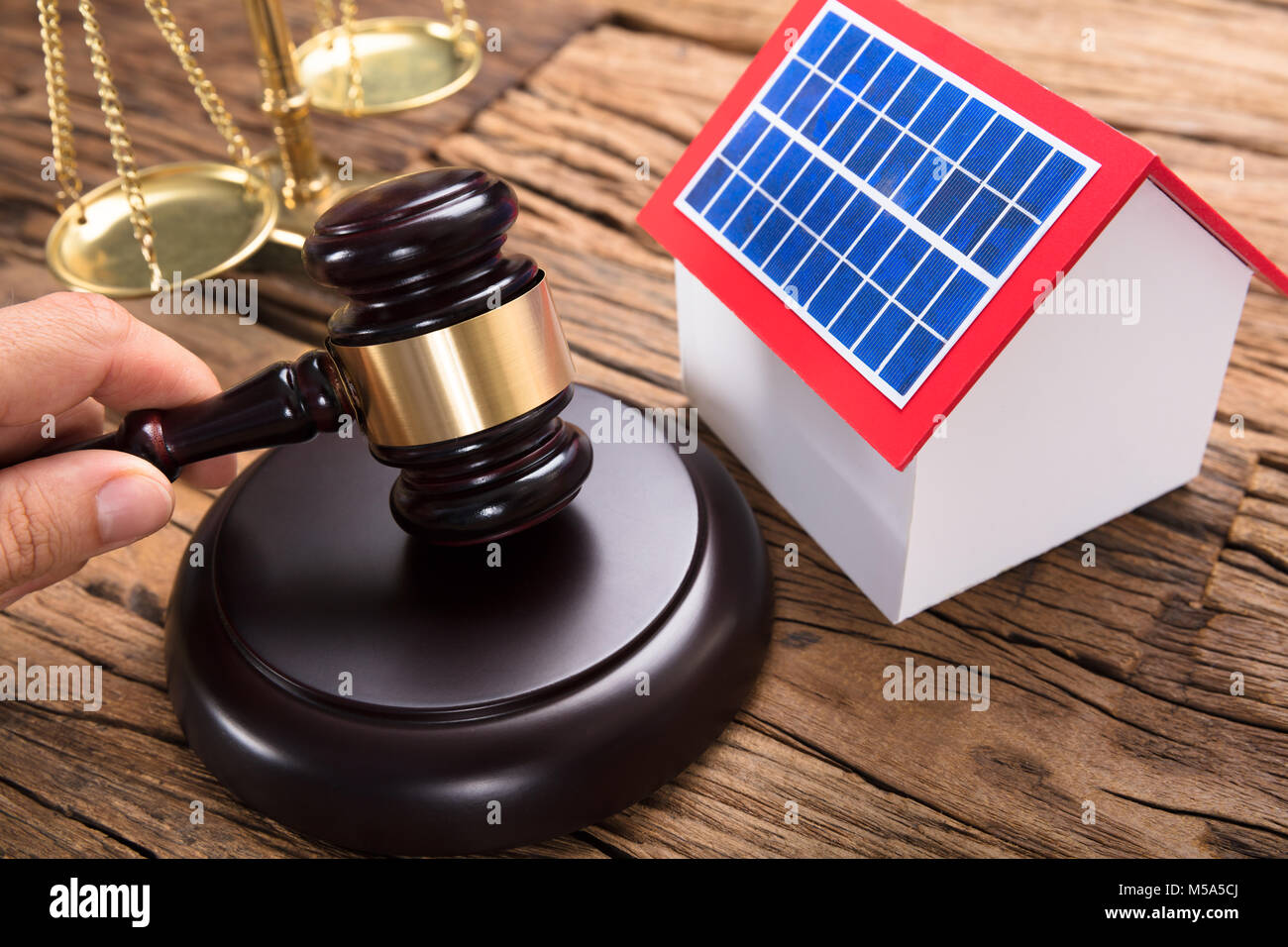 Judge hitting mallet by solar model home and justice scale on wooden table in courtroom Stock