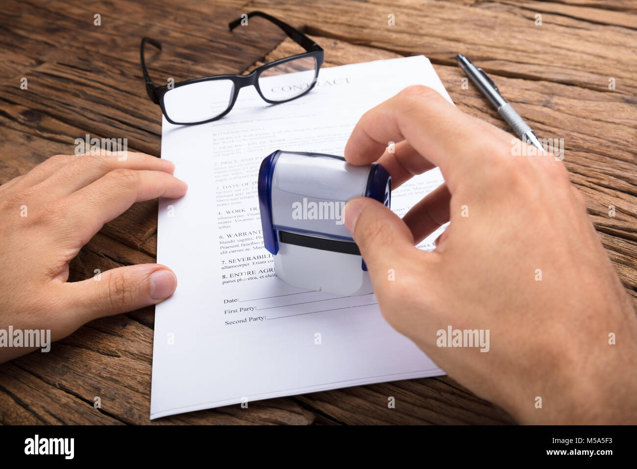Cropped hands of businessman stamping contract paper at wooden table Stock Photo