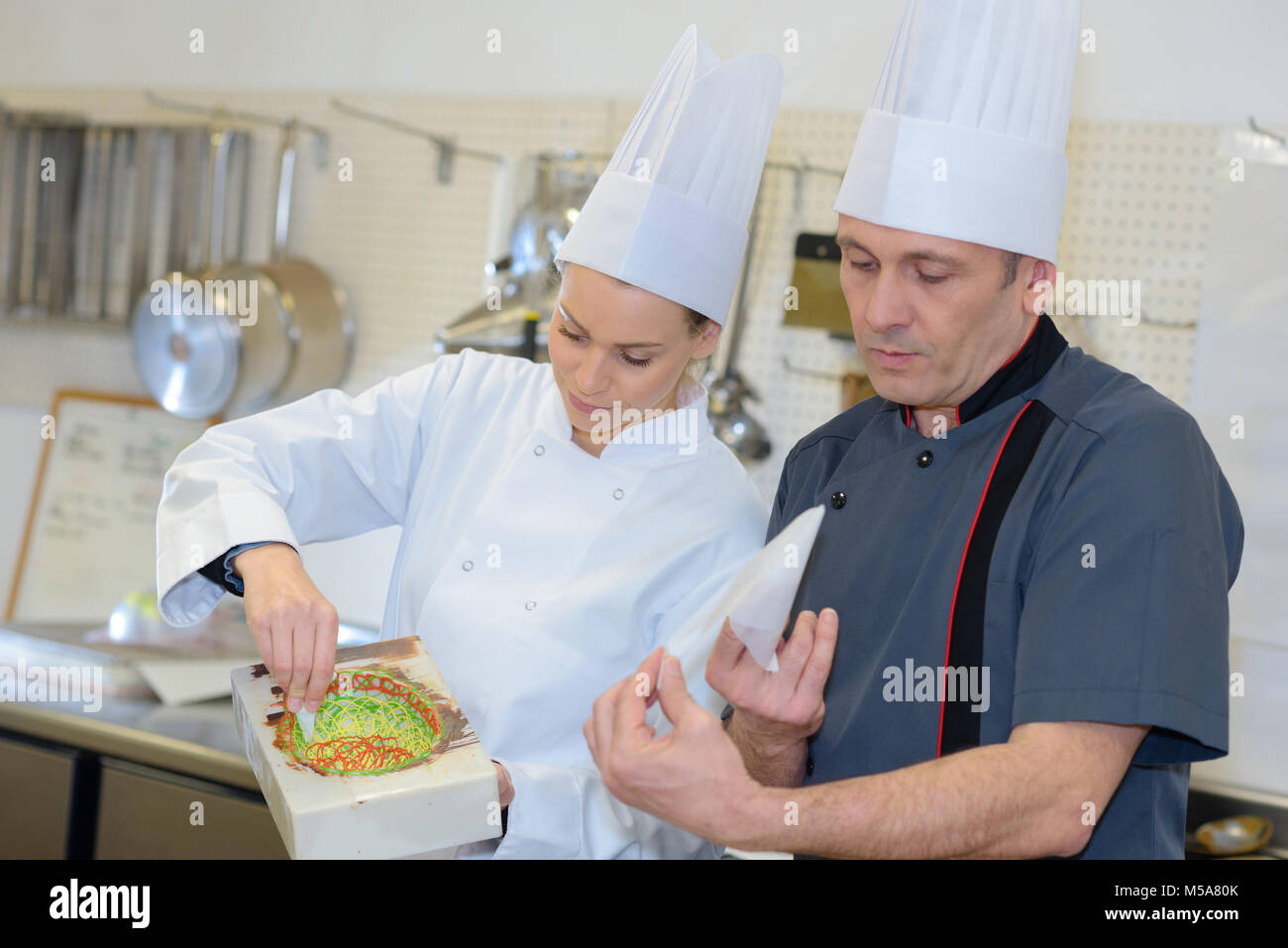pastry chef and assistant in the kitchen decorating a cake Stock Photo ...