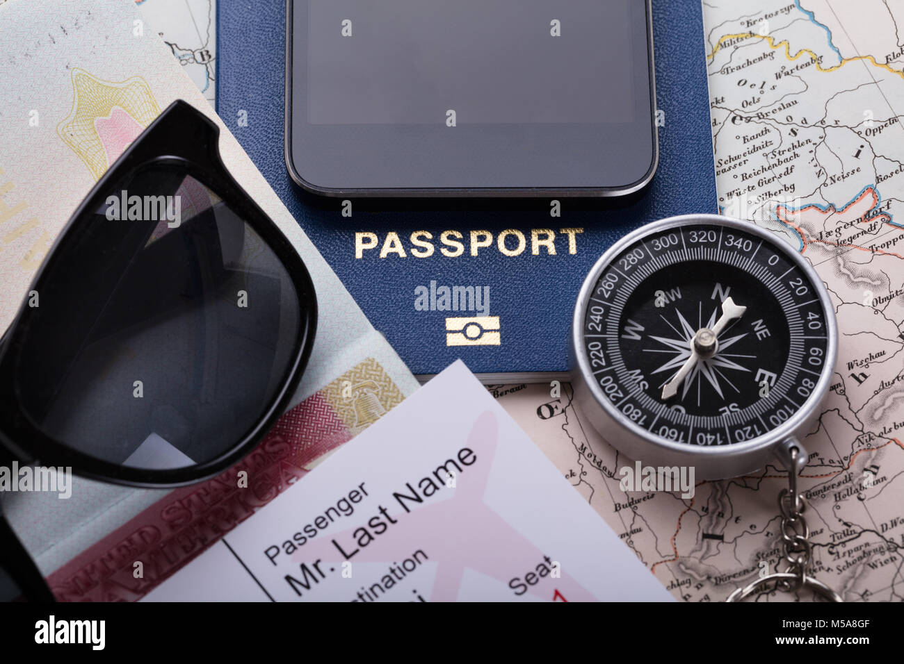 High Angle View Of Smartphone, Boarding Pass Ticket, Passport And Compass On Map Stock Photo