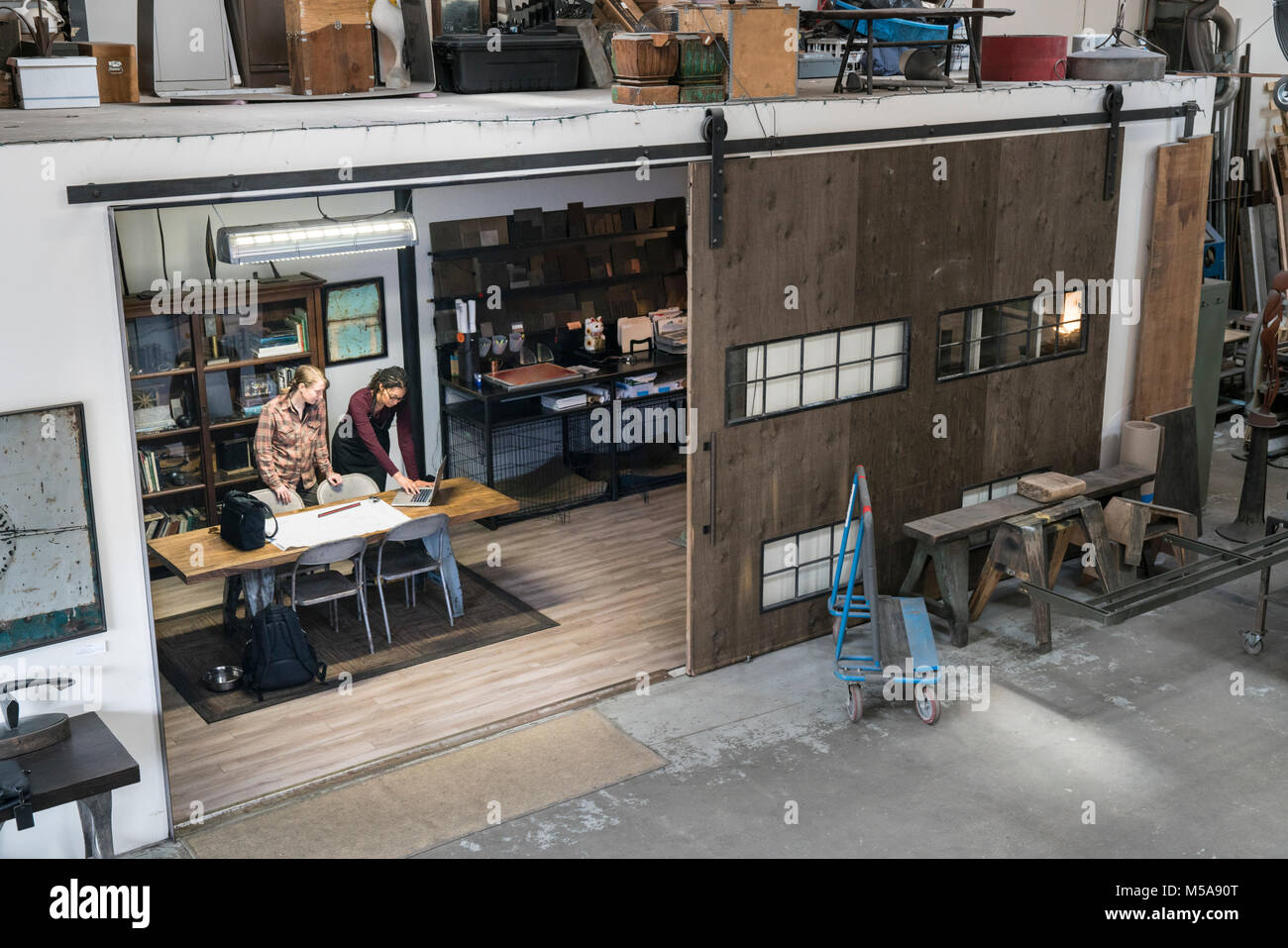 High angle view of two women gathered around table in office area of metal workshop. Stock Photo