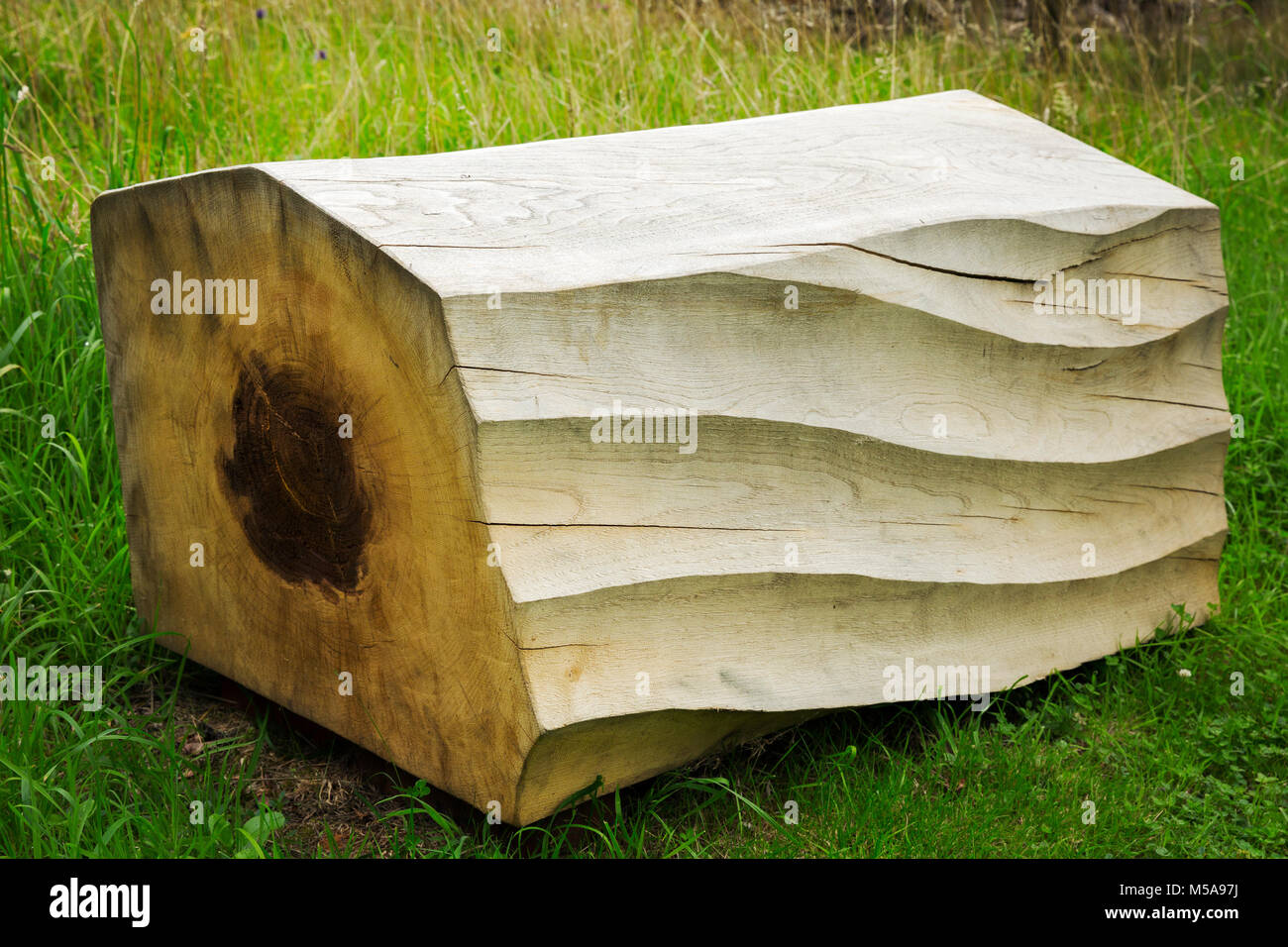 Close up of carved piece of tree trunk with wave pattern lying on grass. Stock Photo