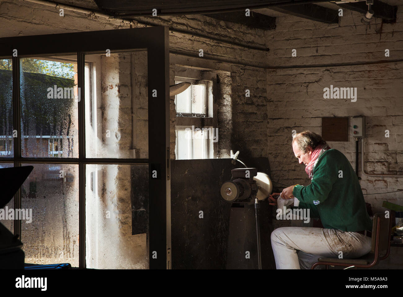 A craftsman sitting in a sharpening the blade of a knife using a surface grinder Stock