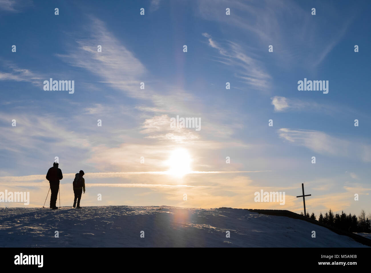 Father and son hiking on snowy mountain Schoeckl to summit cross with nice sunset in Austria Stock Photo