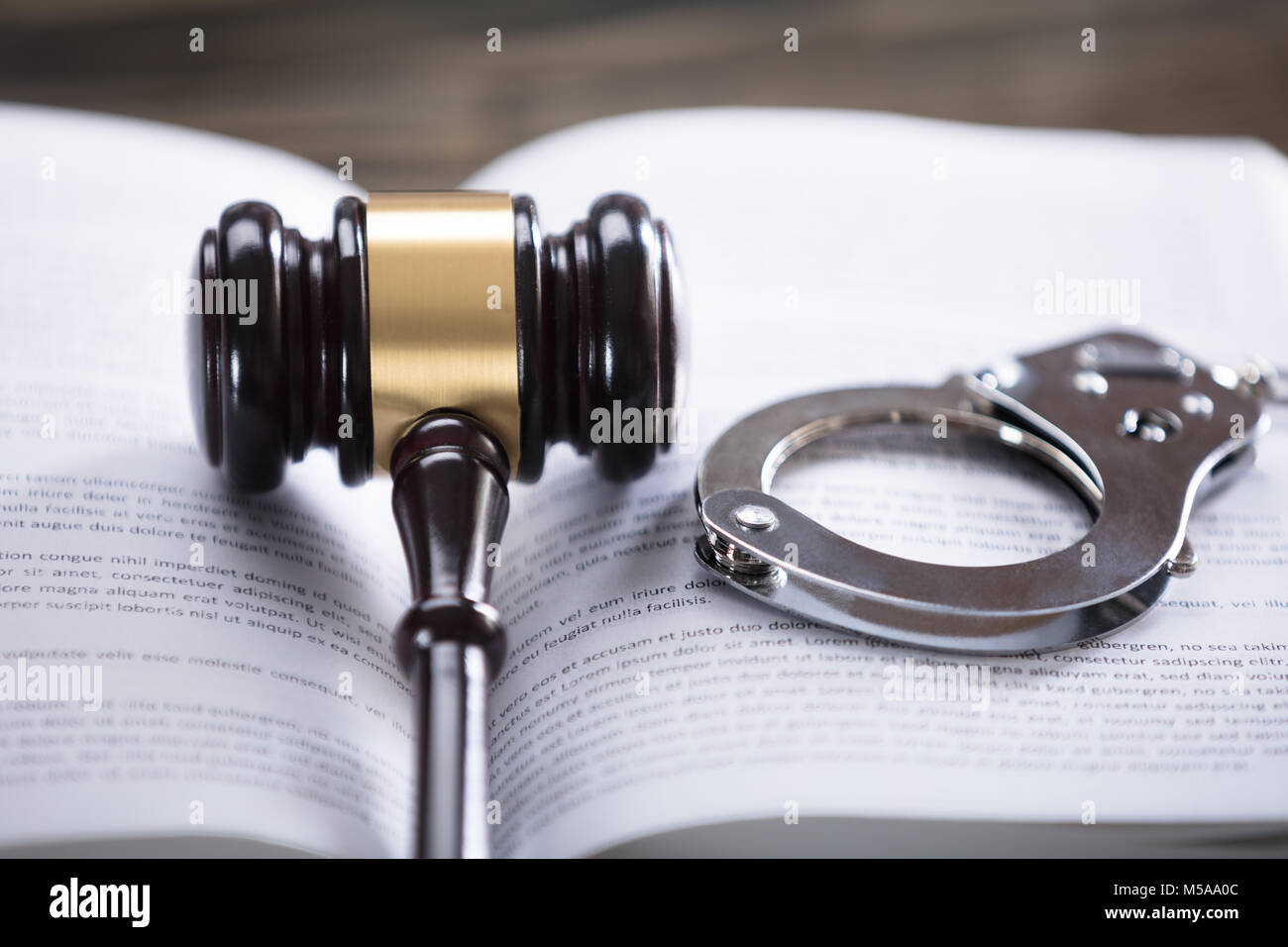 Close-up Of Wooden Mallet And Handcuffs On Law Book In Courtroom Stock Photo