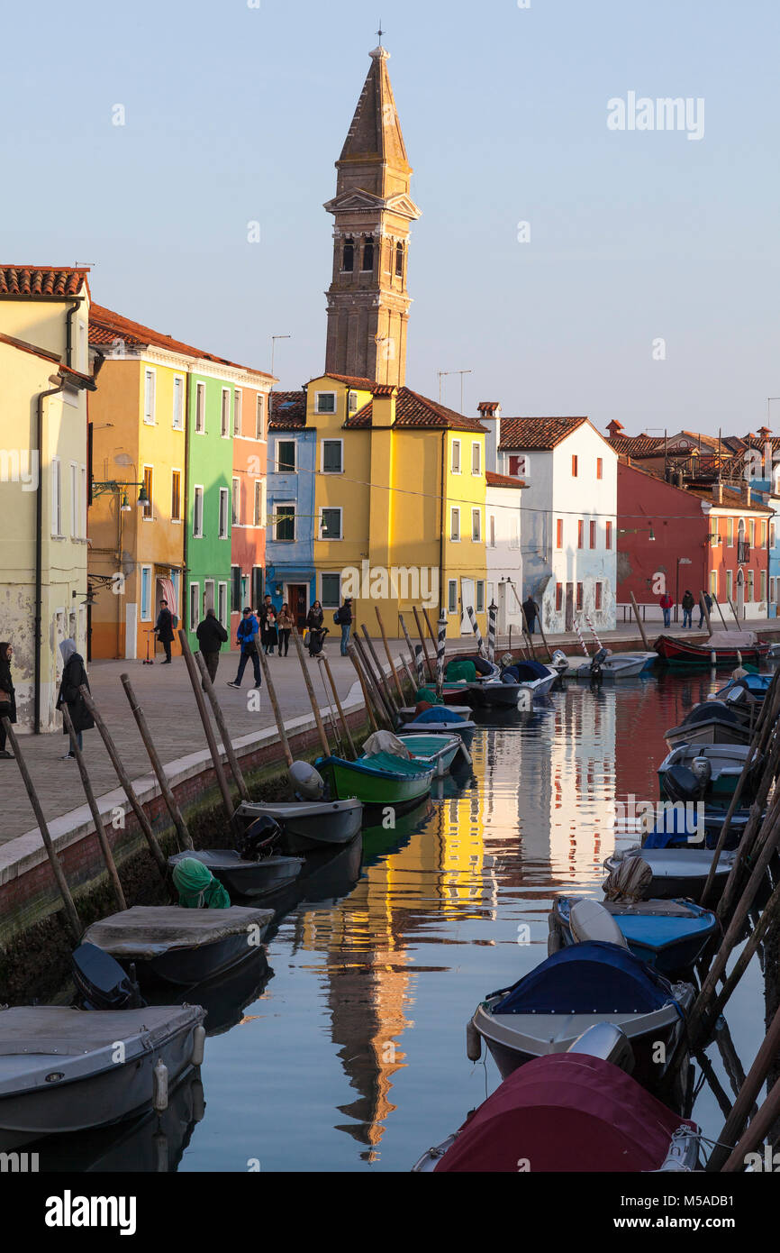 Sunset on Burano Island, venice, Veneto, italy with the bell tower of San Martino church reflected in the canal and people strolling on Fondamenta del Stock Photo