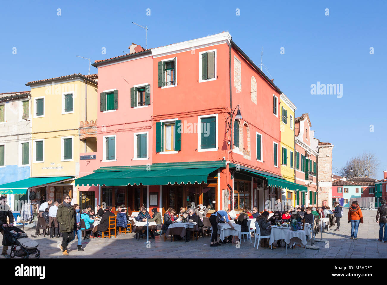Burano, Venice, Veneto, Italy. Tourists dining at a restaurant in Via Baldassare Galuppi and Pizza Baldassare Galuppi on a sunny winter day over the c Stock Photo