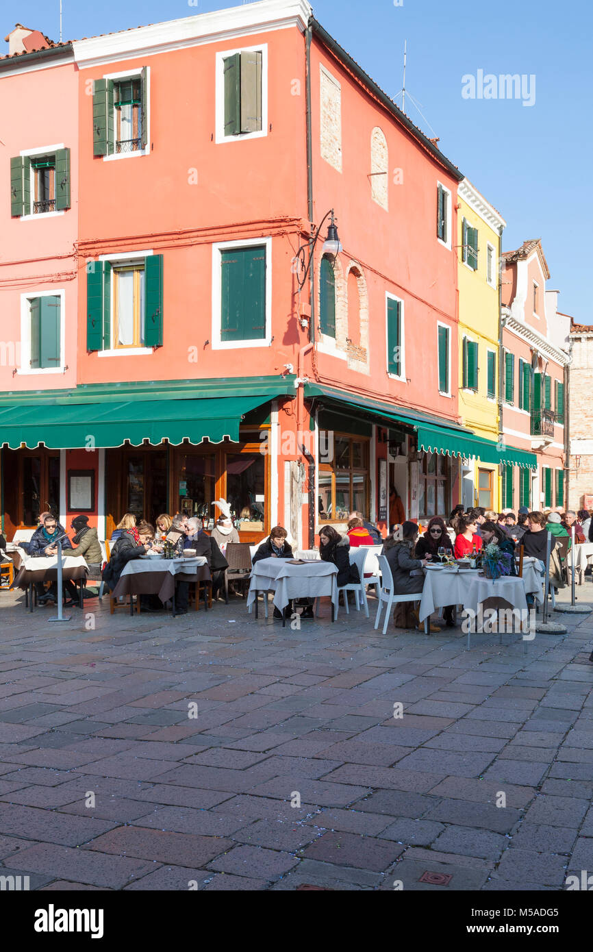 Burano Island, Venice, Veneto, Italy. Diners in Via Baldassare Galuppi sitting at an open air restaurant in the winter sun Stock Photo
