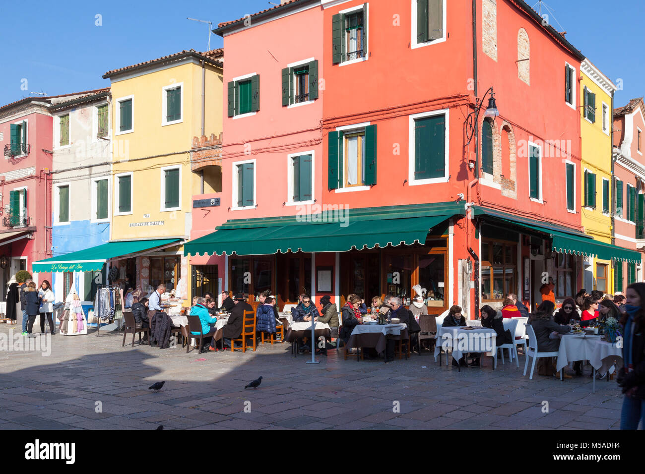 Burano Island, Venice, Veneto, italy. People dining at a corner restaurant on Via Baldassare Galuppi on a sunny winter day with colorful architecture Stock Photo