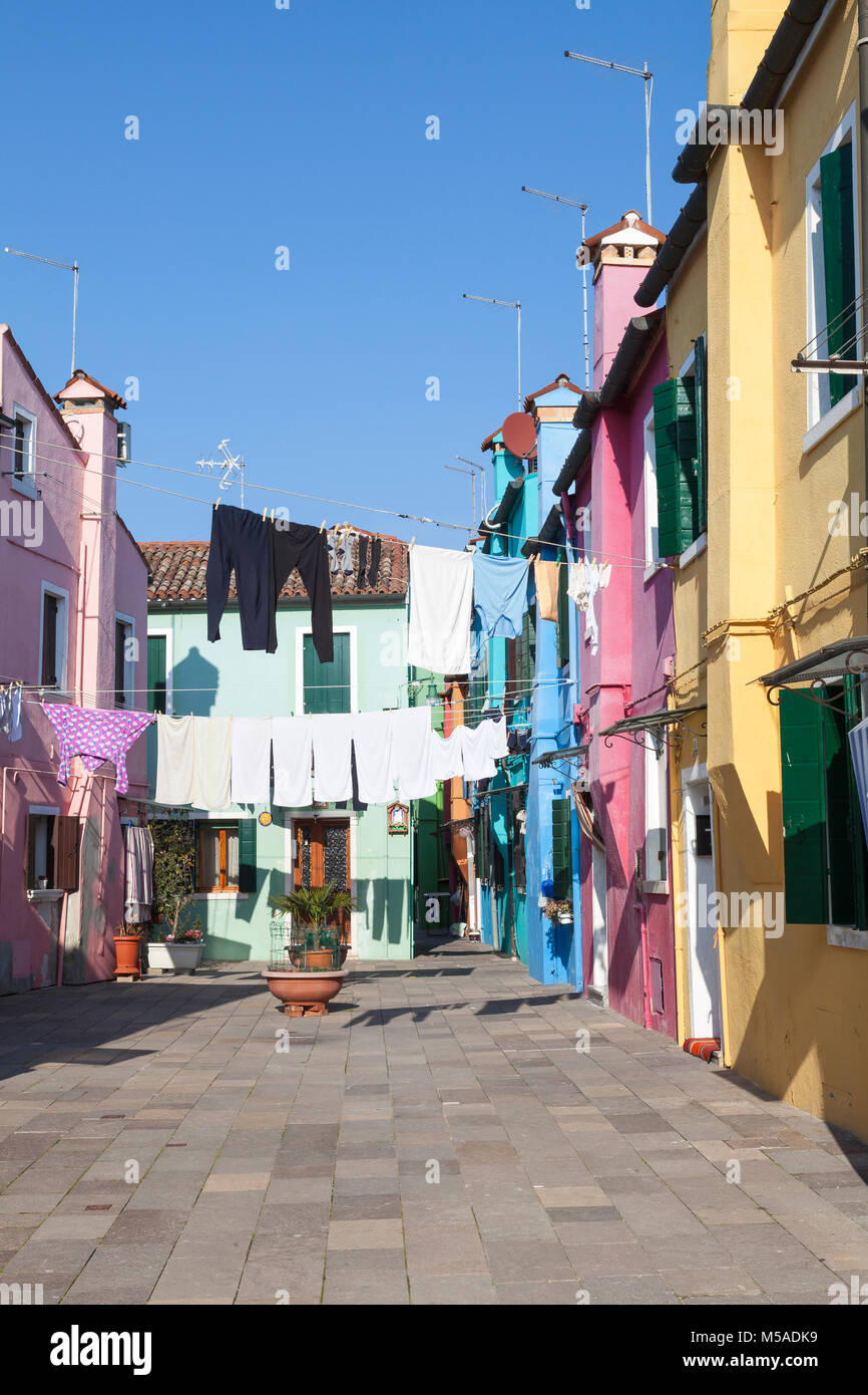 Burano Island, Venice, Veneto, Italy. Washday in a colorful calle or pedestrian walkway lined with multicolored houses with washing drying in the wint Stock Photo
