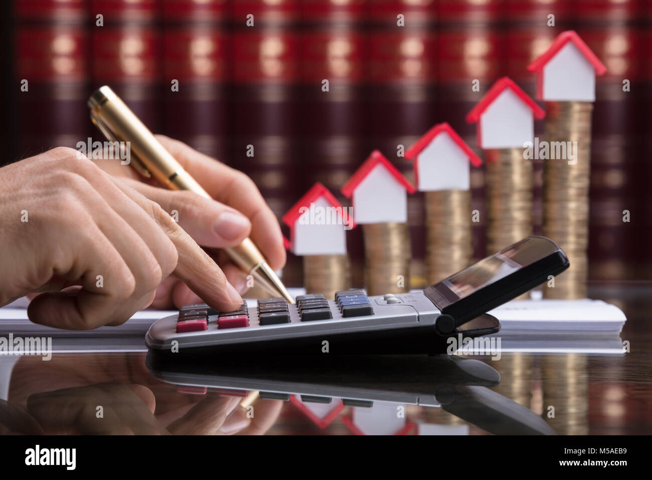 Person Calculating Invoice With Calculator In Front Of Stacked Coins And House Model Stock Photo