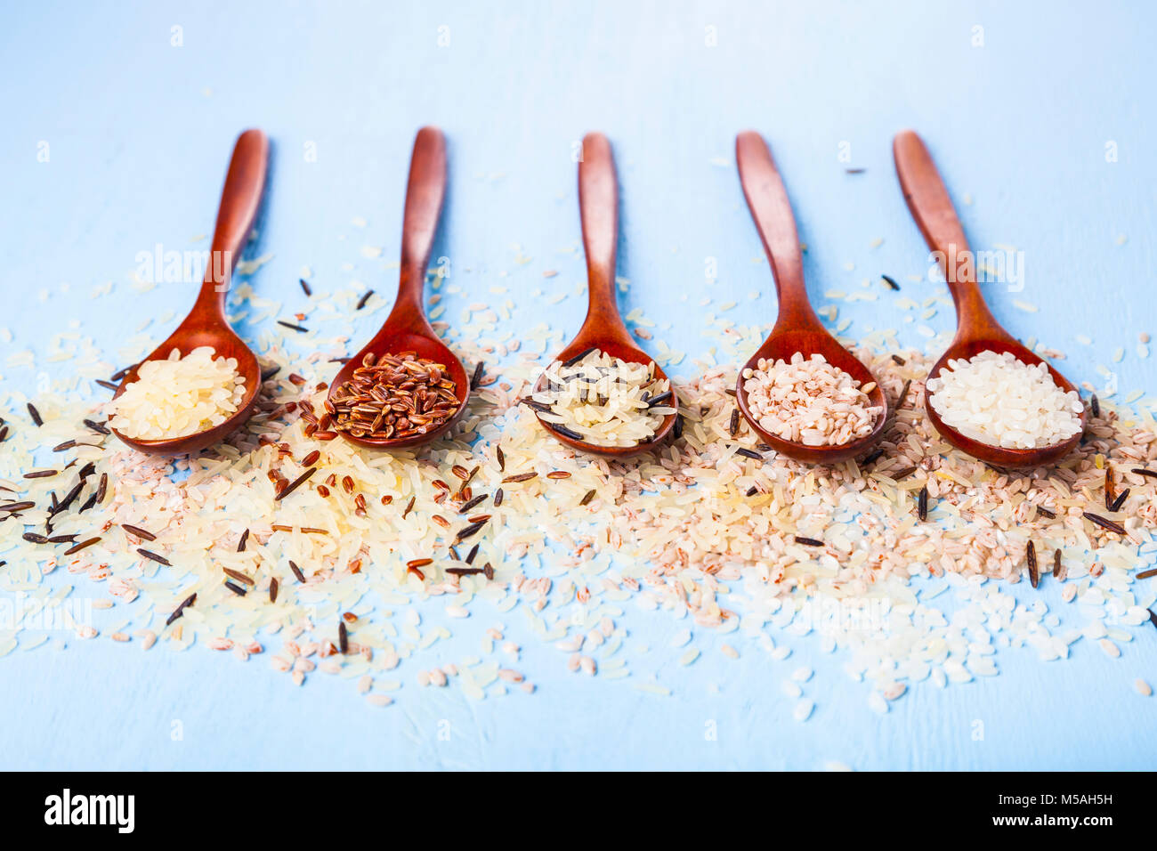 Five spoons with different grades of rice on an old wooden background ...