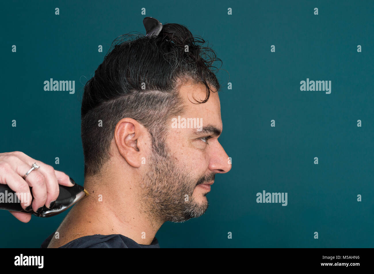 Female hairdresser working with hair clipper, shaving young man's neck Stock Photo