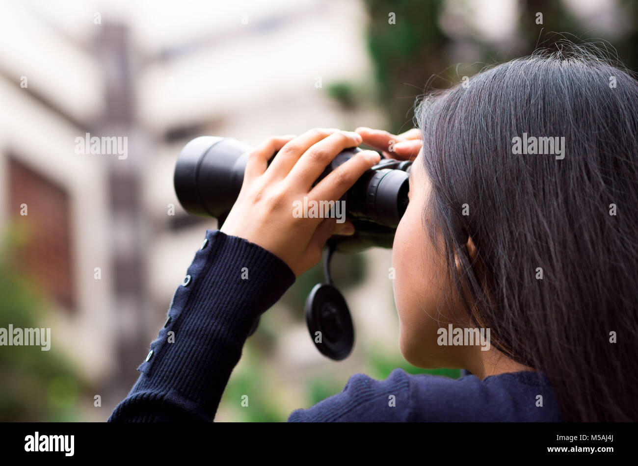 Young woman stalking with a black binoculars in a city background Stock