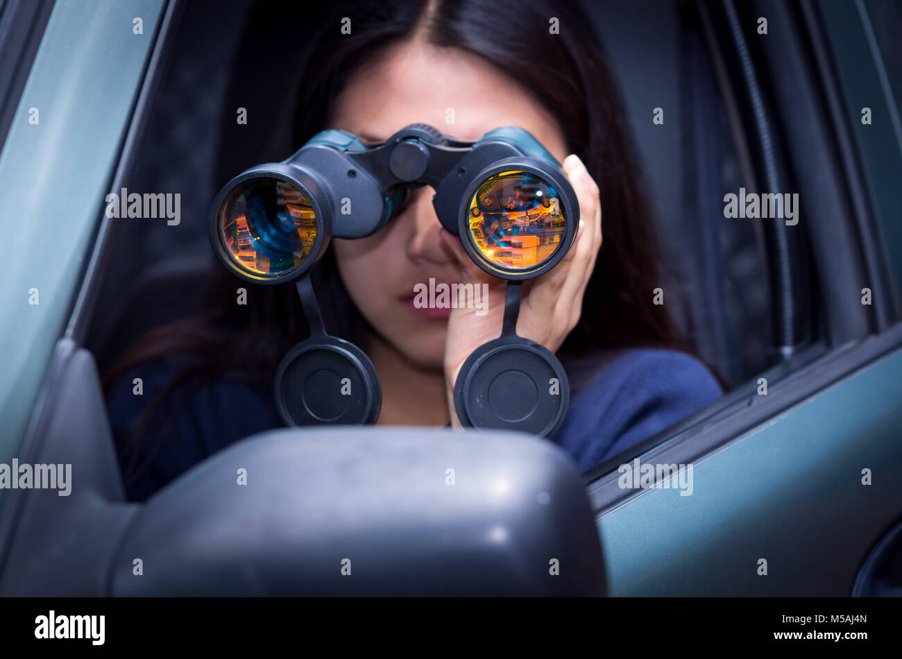 Young woman stalking with a black binoculars inside of her car Stock