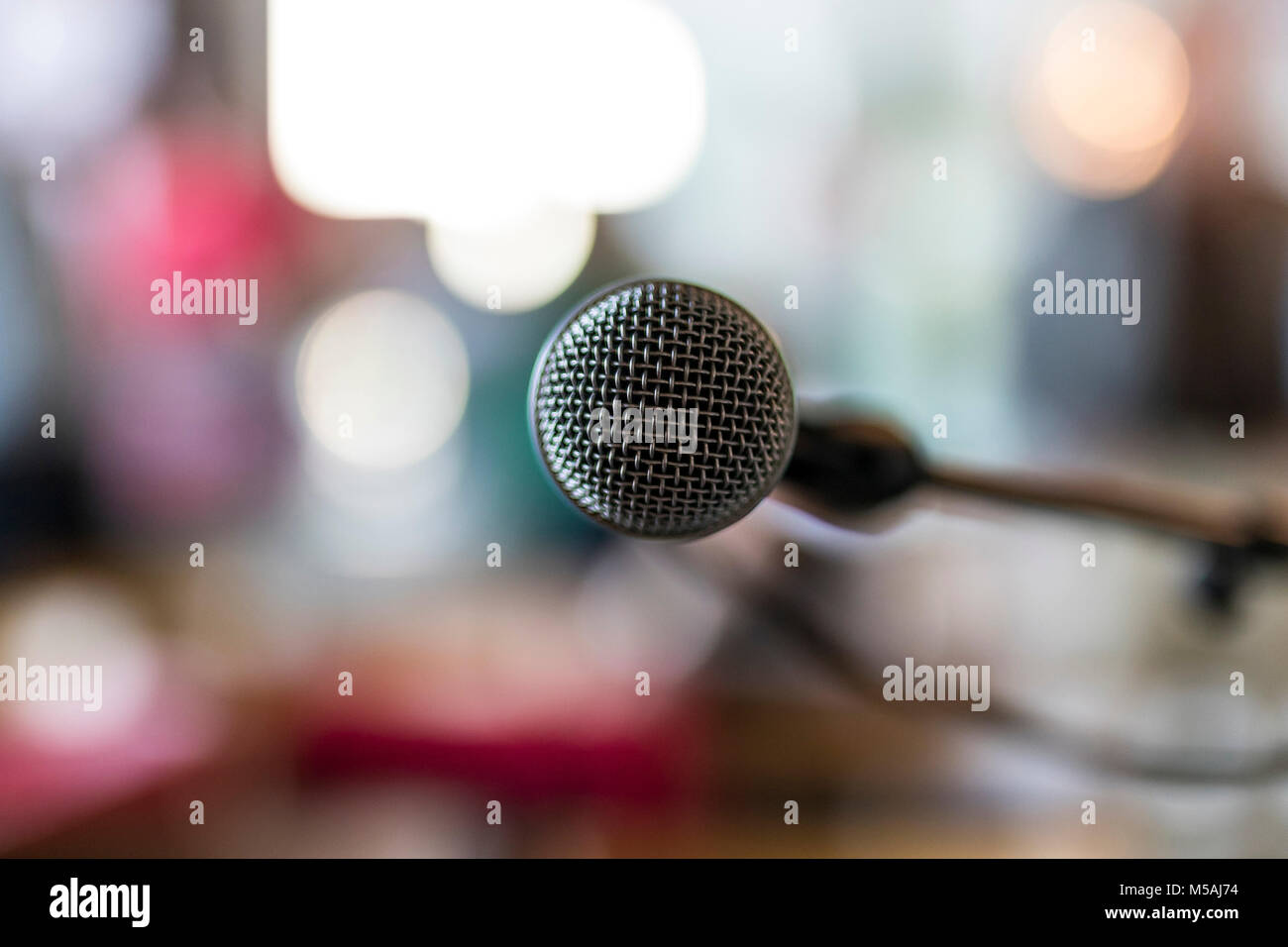 Close up of microphone in concert hall or conference meeting room with blurred abstract lights in background Stock Photo