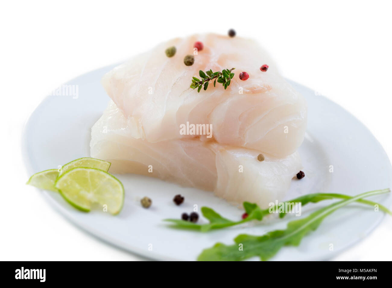 Fresh raw cod fish fillet on a plate with parsley and lemon isolated against white background Stock Photo