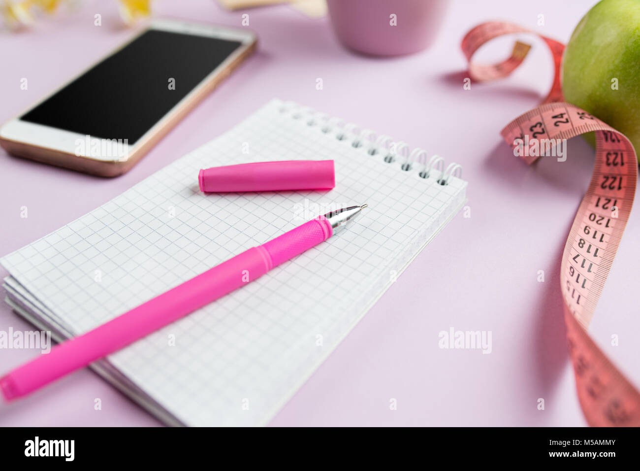 side view of green apple, measuring tape, mobile phone, pen and open notebook. Fitness Concept