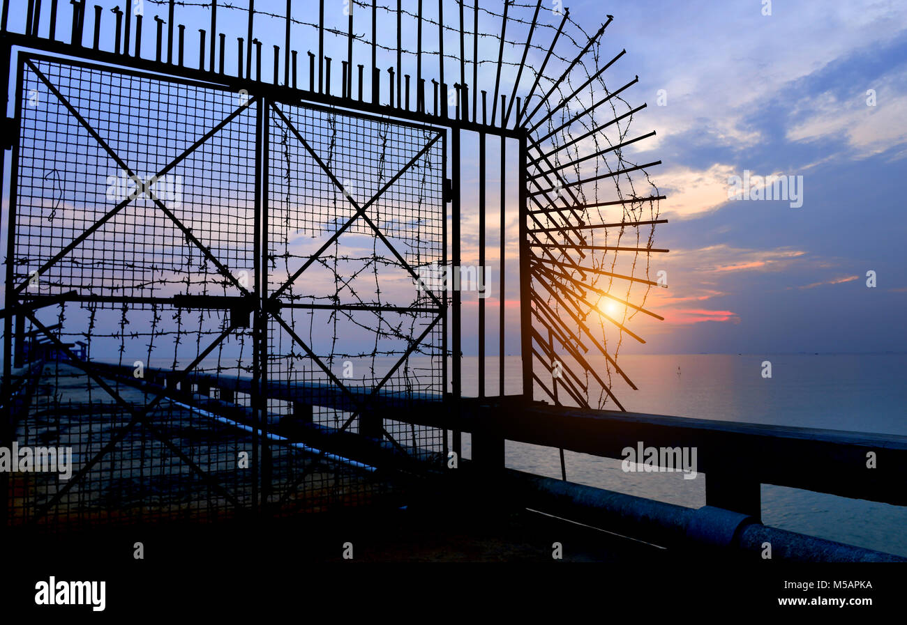 The silhouette of old metal and rusty door on the sea bridge photo in  outdoor sunset low lighting and dark shadow in twilight sky . Stock Photo