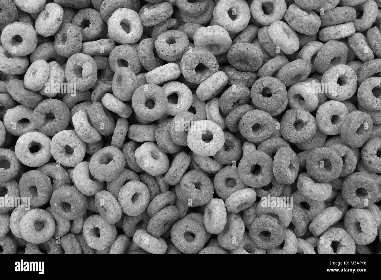 Multigrain hoops breakfast cereal - rings of wheat, barley, rice, oats and maize - as an abstract background texture - monochrome processing Stock Photo