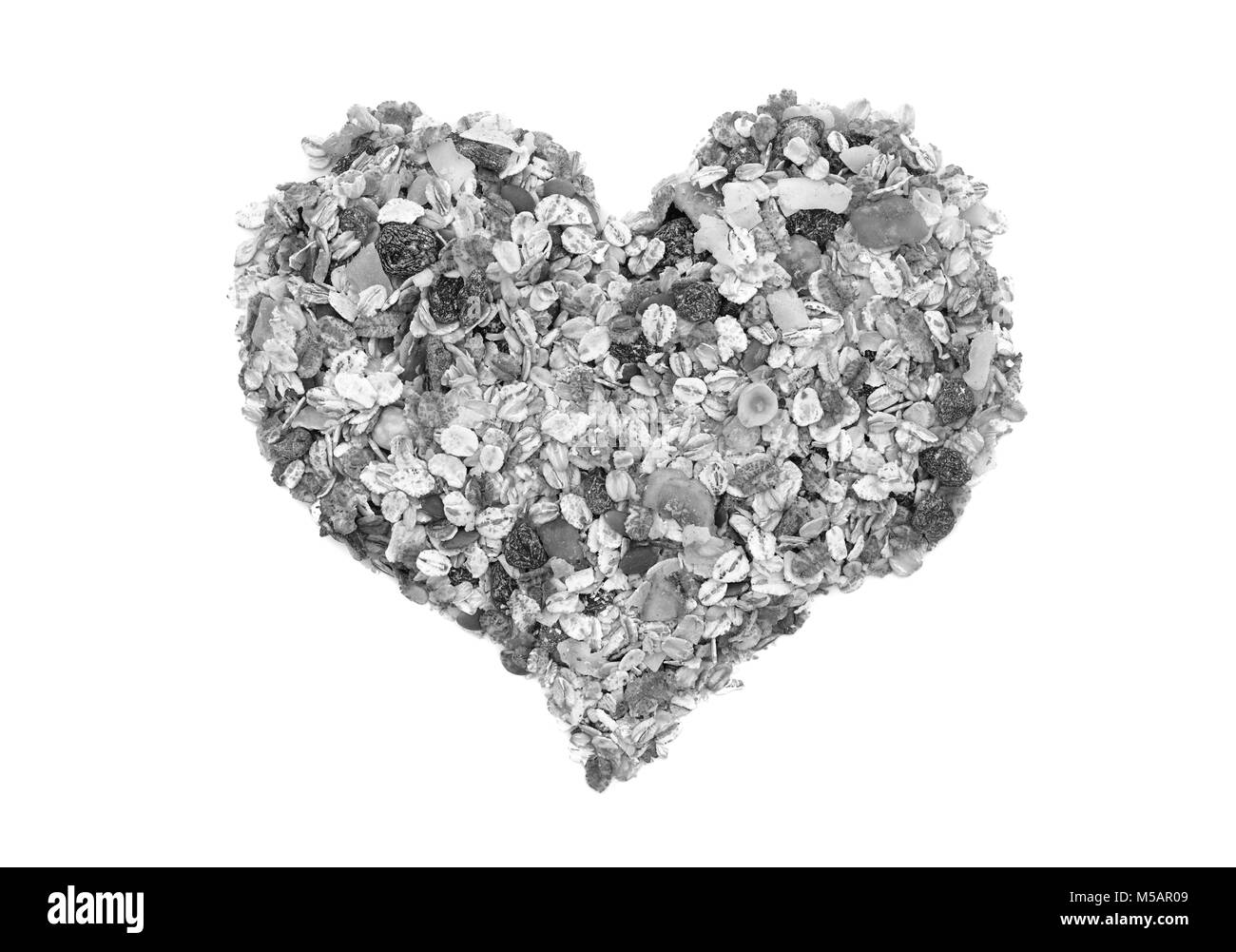 Muesli cereal grains, seeds, fruit and nut in a heart shape, isolated on a white background - monochrome processing Stock Photo