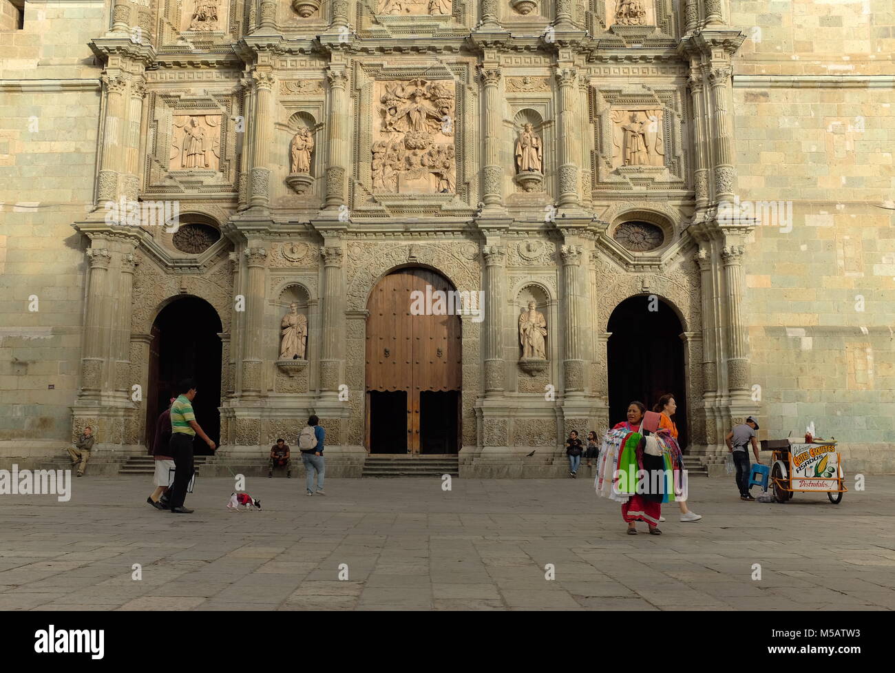 People individually making their way through the day as their paths cross in front of the iconic Cathedral of Our Lady of the Assumption in Oaxaca. Stock Photo