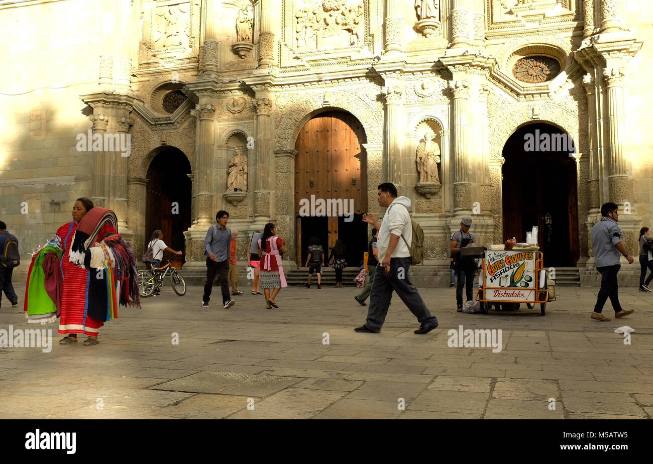 People individually making their way through the day as their paths cross in front of the iconic Cathedral of Our Lady of the Assumption in Oaxaca. Stock Photo