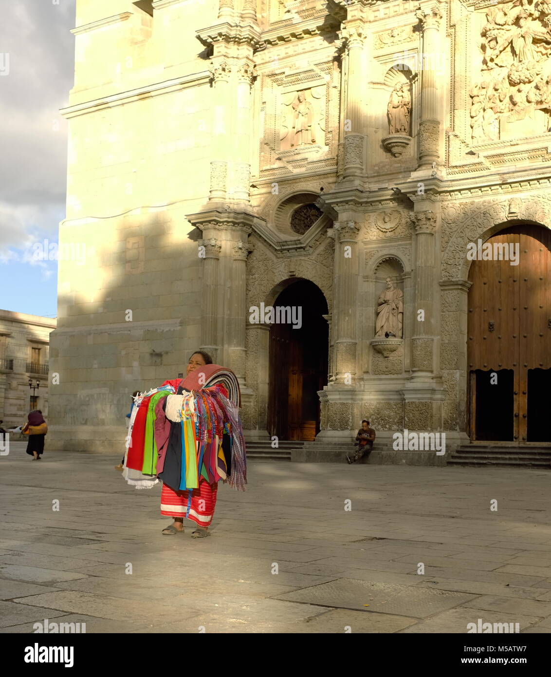 The sun sets majestically on a woman standing stoically in front of the Cathedral of Our Lady of the Assumption in Oaxaca, Mexico. Stock Photo