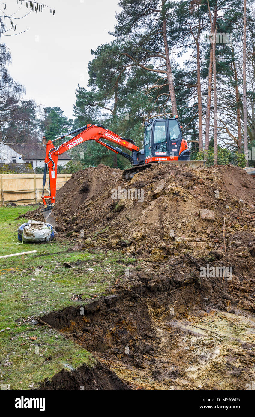Large orange heavy plant mechanical digger parked on an earth mound after digging excavations for foundations of a new residential development Stock Photo