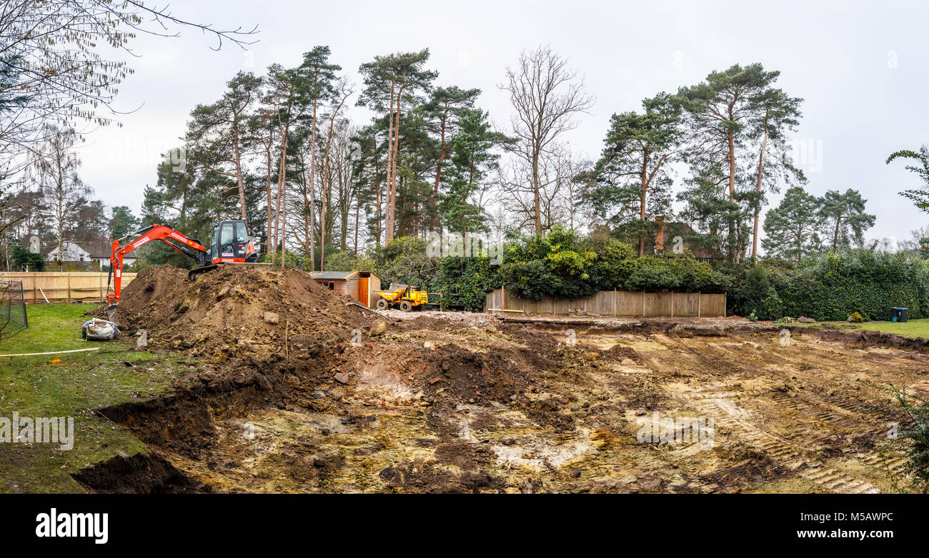 Large orange heavy plant mechanical digger parked on an earth mound after digging excavations for foundations of a new residential development Stock Photo