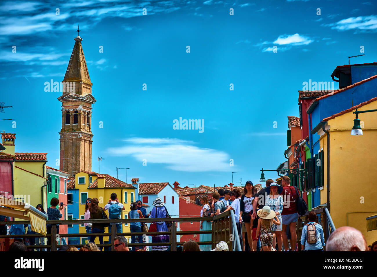 BURANO, ITALY - MAY 21, 2017: Tourists walking on a bridge in Burano with the Leaning Bell Tower in the background. Stock Photo