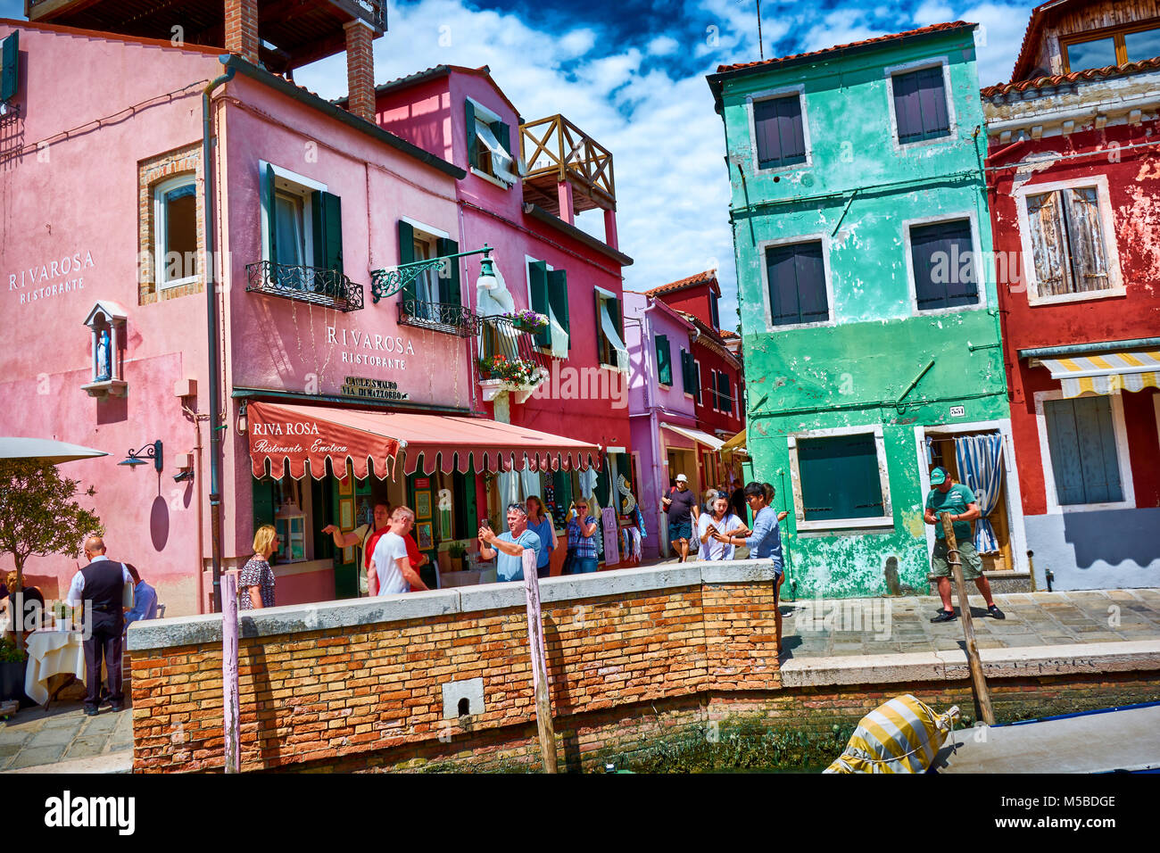 BURANO, ITALY - MAY 21, 2017: View of colorful buildings and stores on the streets surrounded by tourists in Burano. Stock Photo