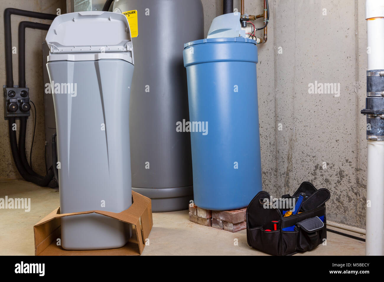 New water softening unit or tank ready alongside the old one for installation to replace it in a utility room with a portable tool kit in a box on the Stock Photo