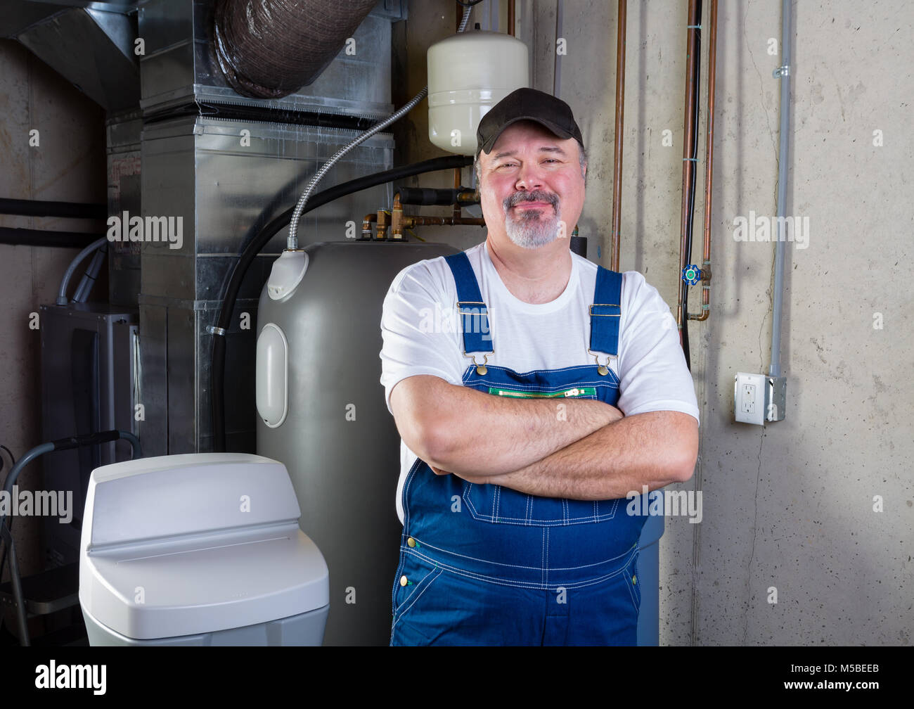 Competent trustworthy workman or home installer standing in a utility room with folded arms smiling at the camera Stock Photo