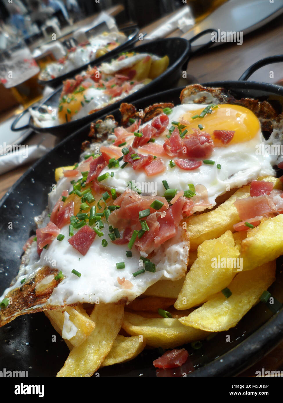 A dish of fried potato chips/fries topped with fried eggs, bacon and