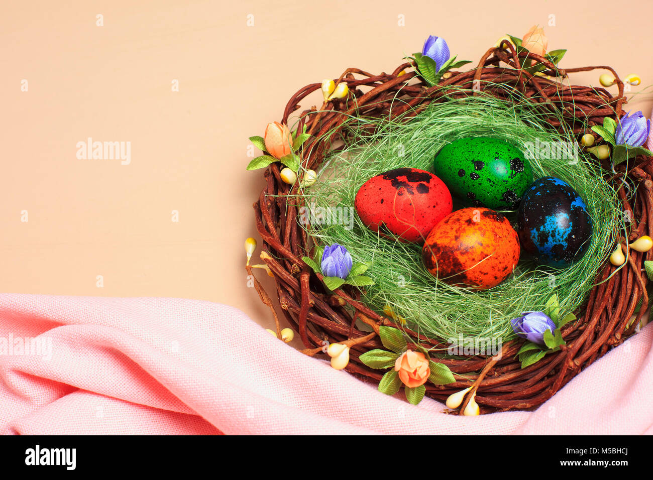 Colorful painted quail eggs in a nest on a beige background and pink ...
