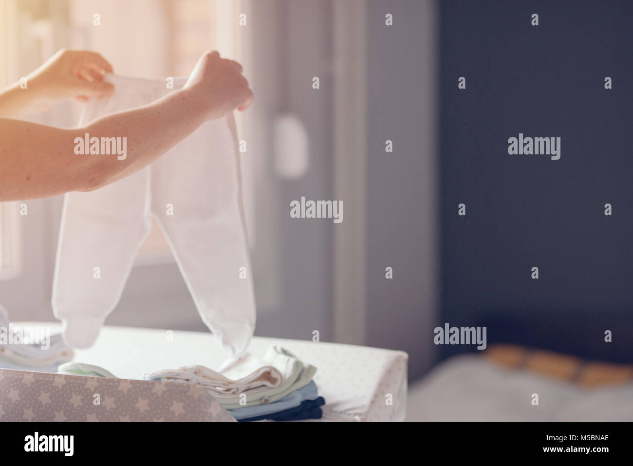 Mother sorting newborn baby clothing for ironing at home as part of everyday routine in child care, selective focus Stock Photo