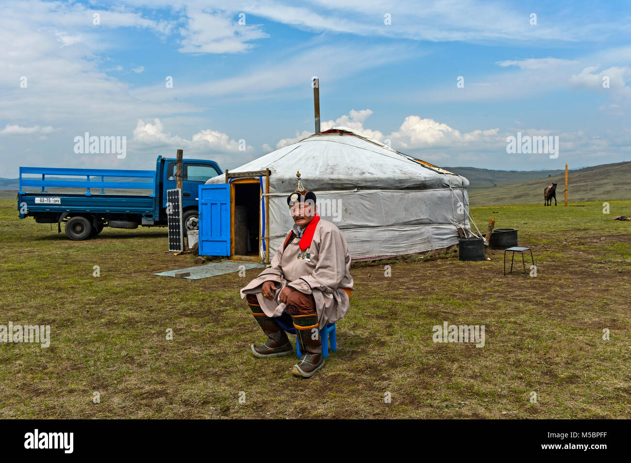 Elderly male nomad in traditional dress sitting in front of his yurt, Mongolia Stock Photo